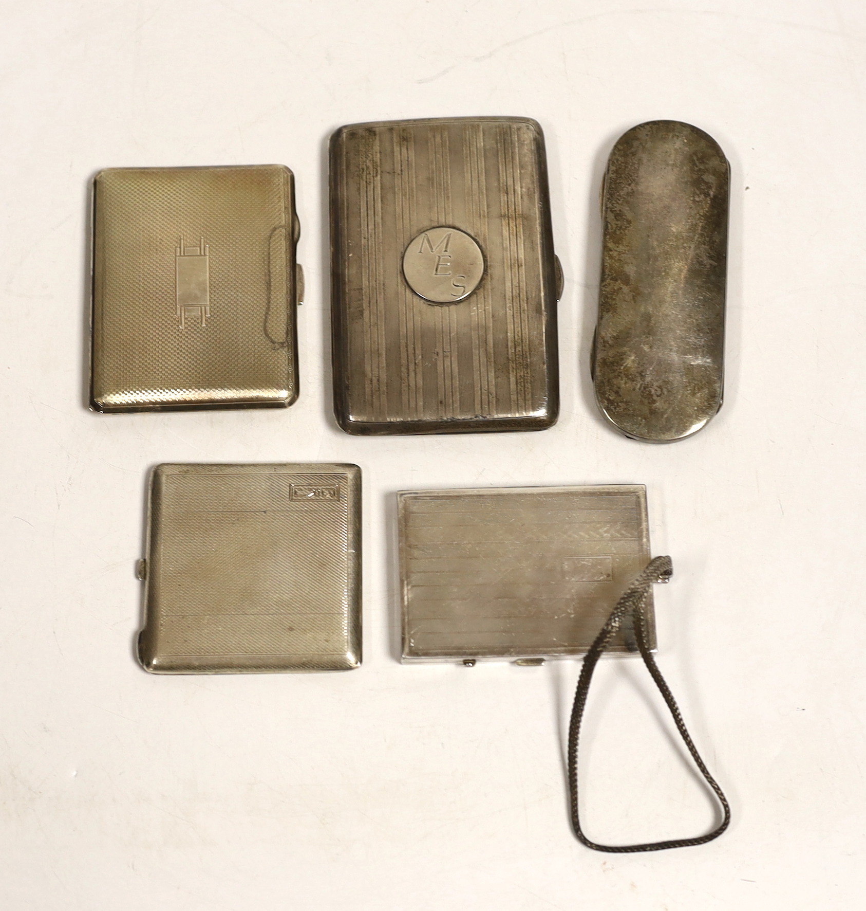Two George V engine turned silver compacts, largest 83mm, a silver mounted aide memoire wallet, a silver spectacles case and a base metal compact.